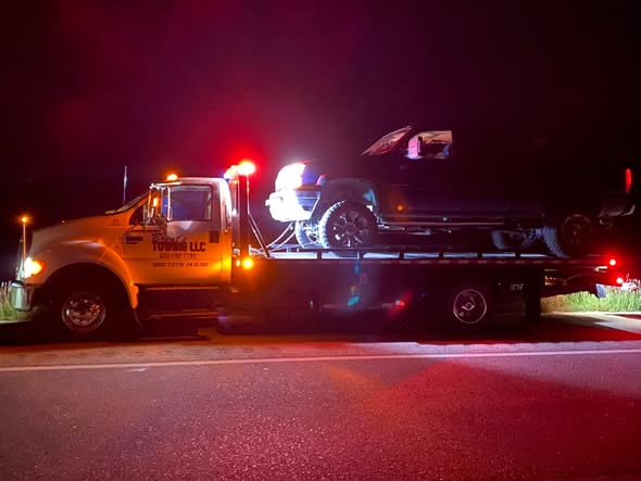 Tow truck with emergency lights loading a pickup truck at night
