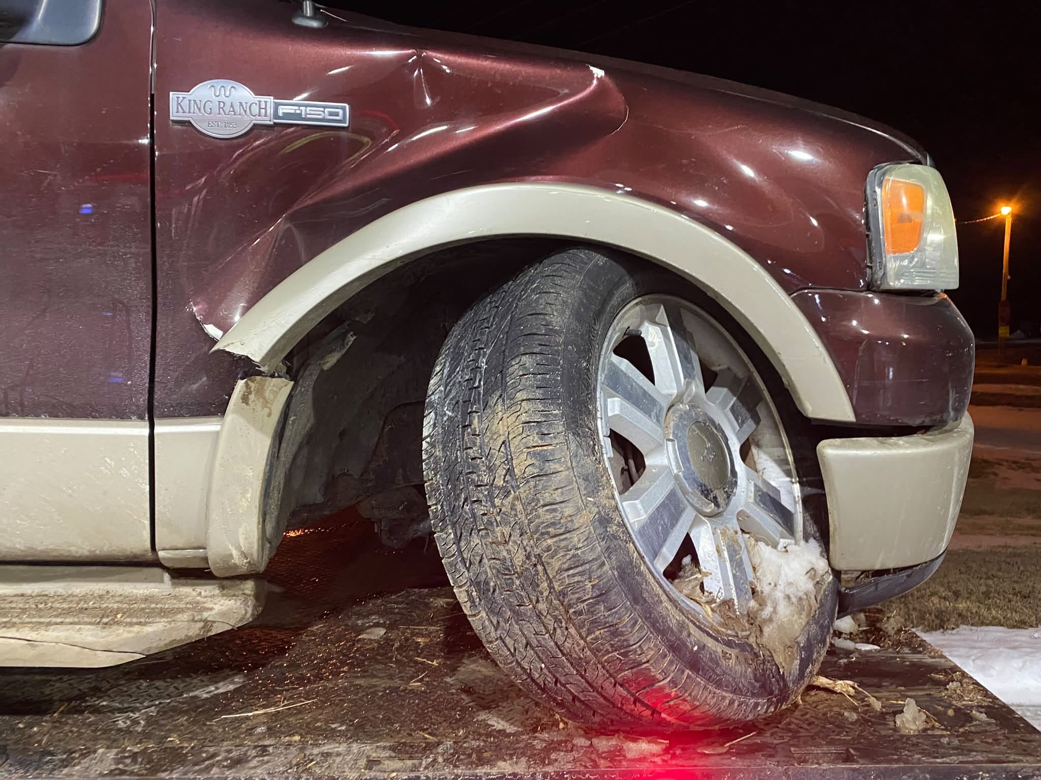 Close-up of collision damage to a truck's front fender and wheel roadside at night